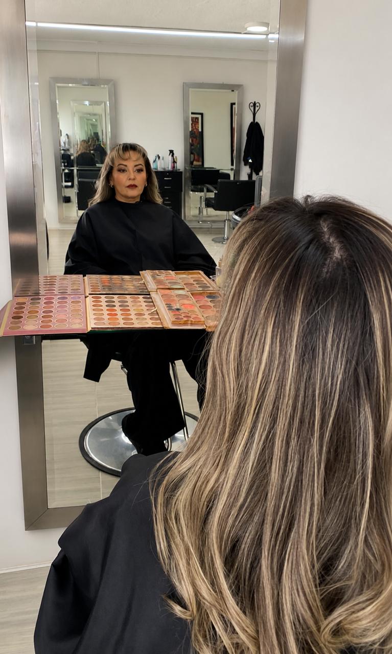 Clienta con balayage frente al espejo y paleta de maquillaje